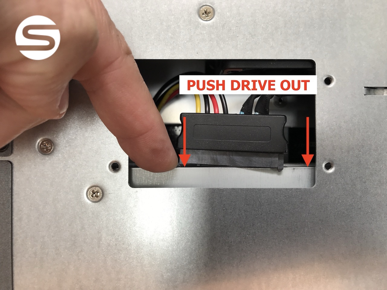 A finger pushing the rear of the drive outward through the inspection panel to free it from the chassis